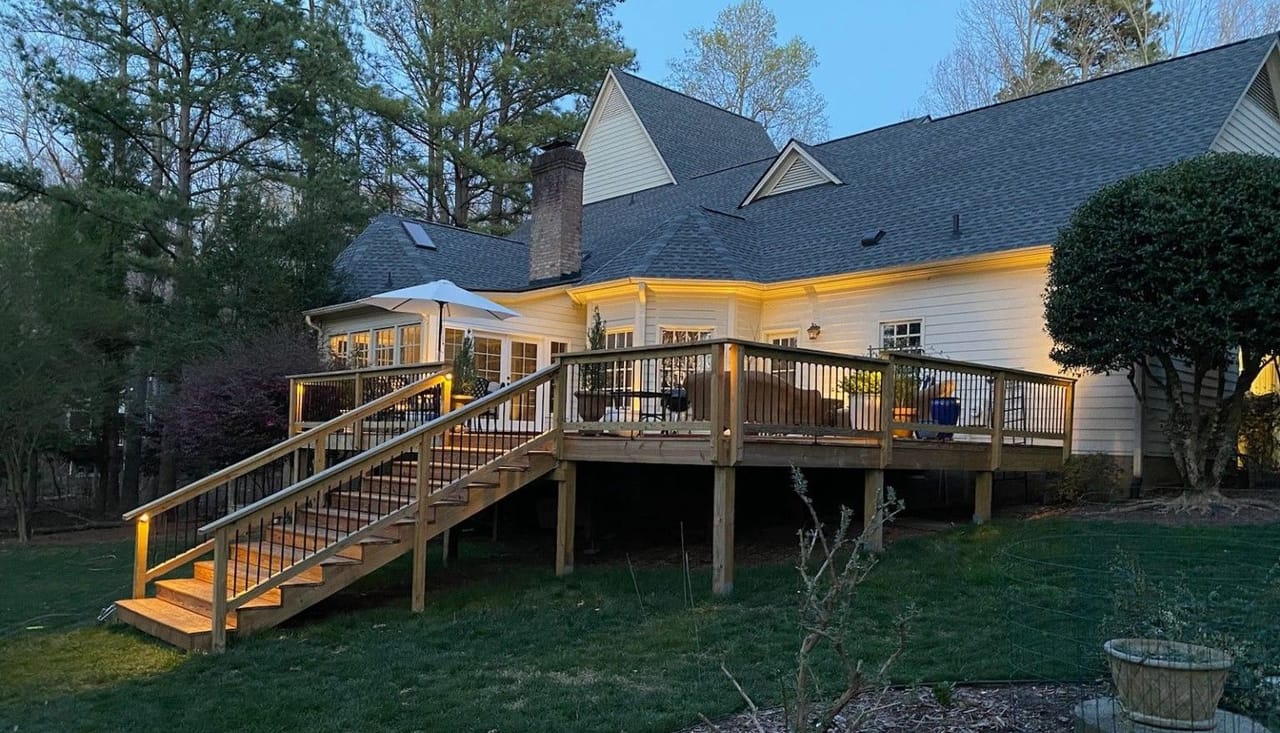 Raised wood deck and staircase with warm post lights at twilight, cream house glowing under the eaves in Wake County