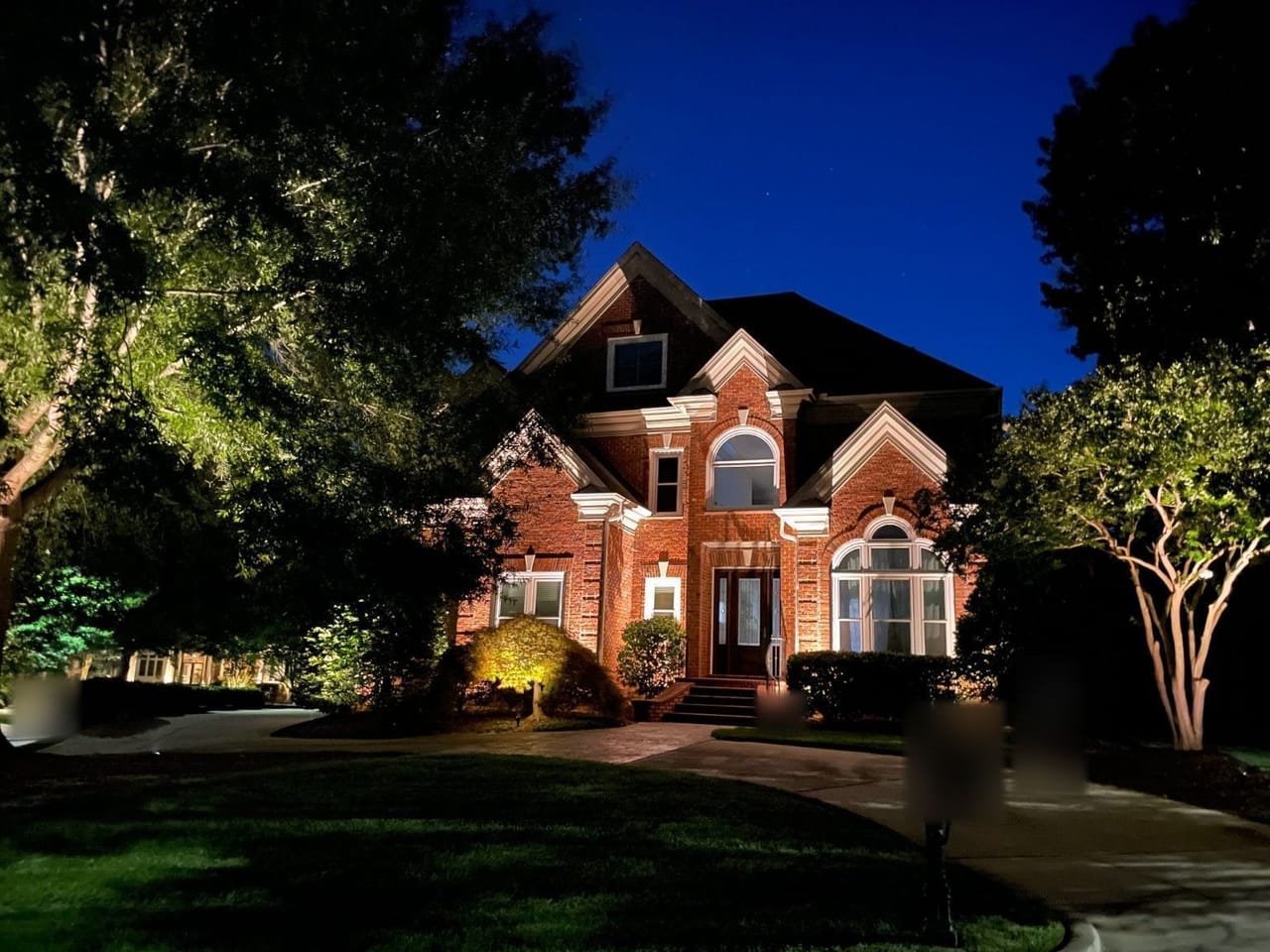 Brick two-story home with uplit facade, crape myrtle and front-yard trees at night in Wake County