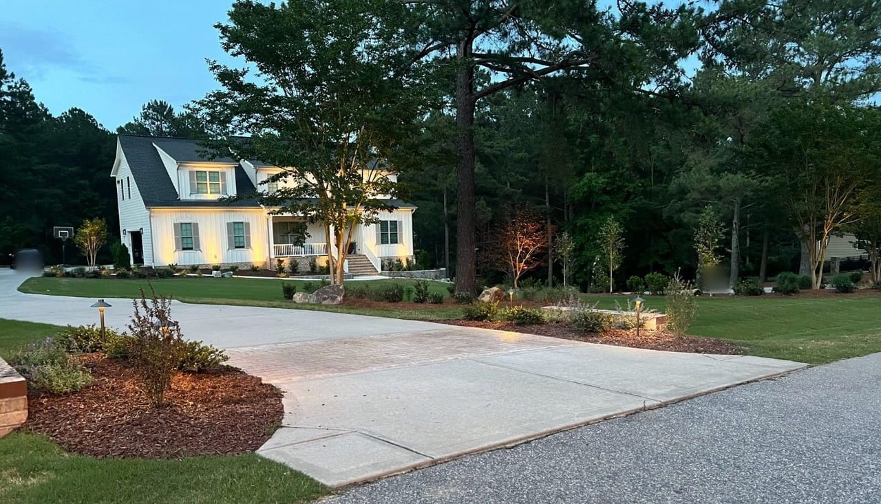 White farmhouse-style home with uplit facade and trees, brass path lights along the driveway at dusk in Wake County