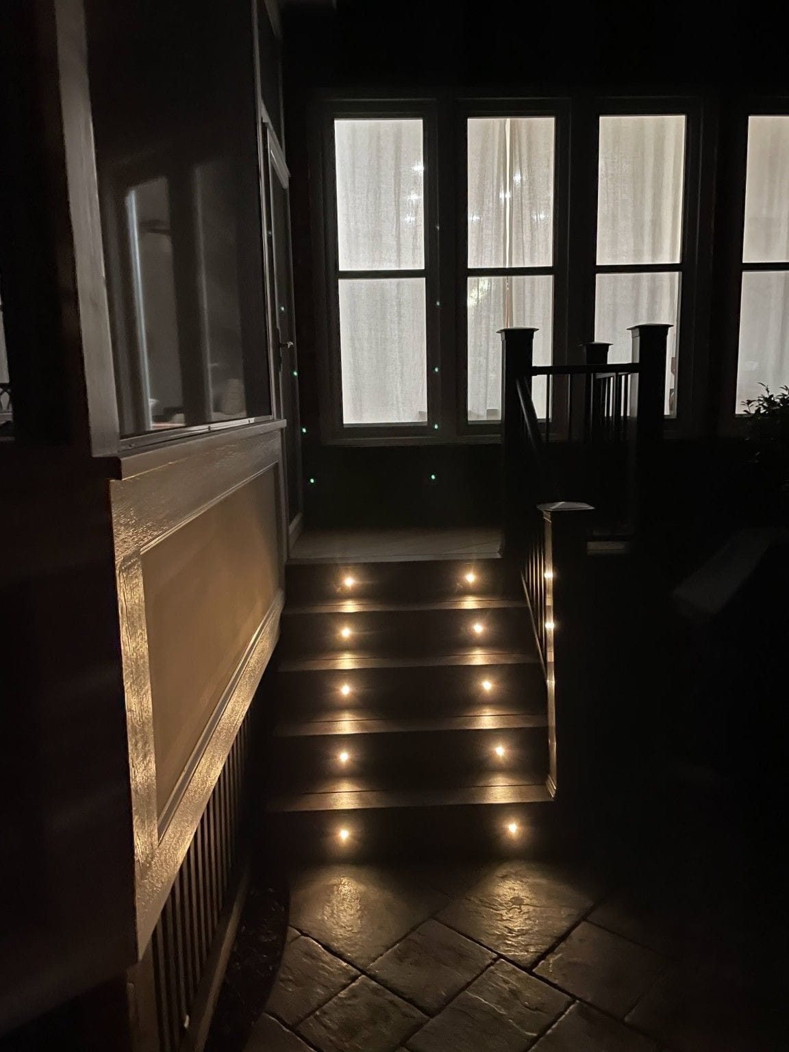 Dark composite deck stairs with round recessed riser lights leading up to a screened porch at night in Wake County
