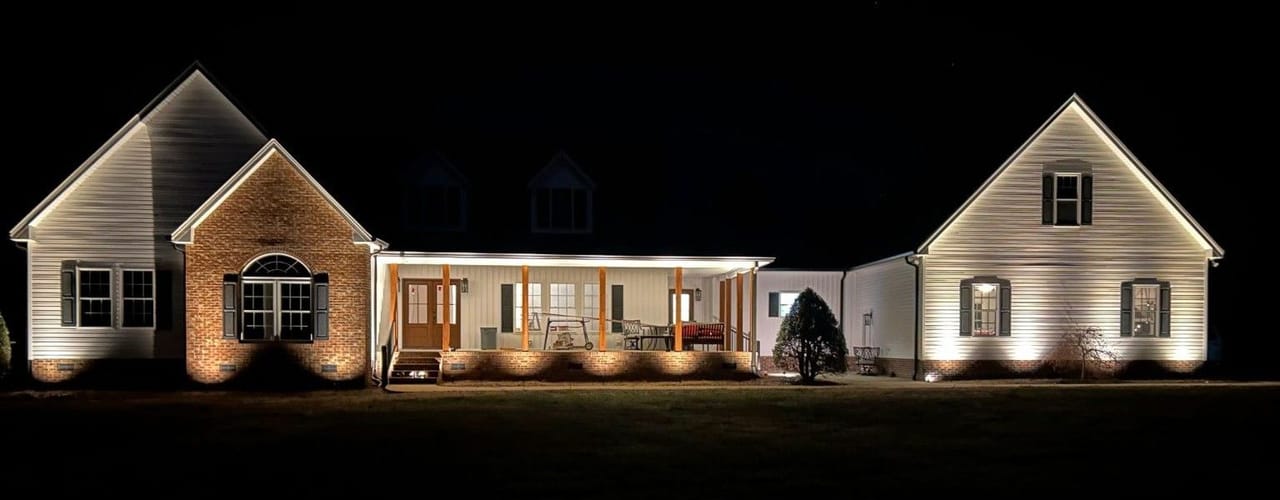 Brick and siding home with foundation uplights grazing the gables and porch at night in Wake County